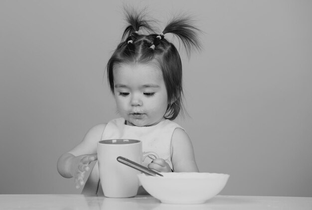 Bebés comiendo alimentos saludables para la primera comida del bebé que el niño come solo con una taza