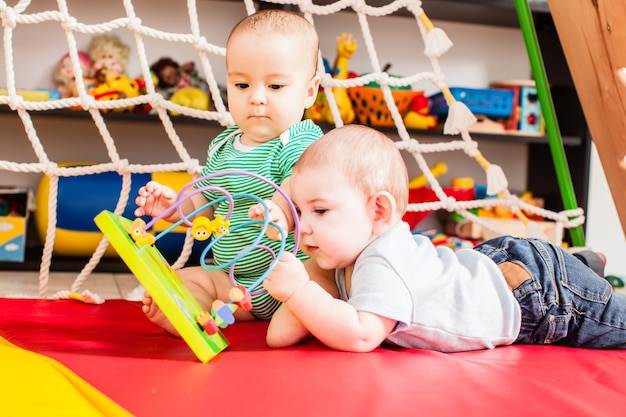 Bebês de dois meninos espertos brincando com um brinquedo na sala de jogos