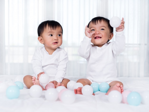 Bebés gemelos alegres jugando a la pelota de color en la cama