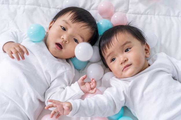 Bebês gêmeos alegres jogando bola colorida na cama