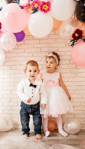 Bebés lindos - niño y niña están tomados de la mano alrededor de los globos. El bebé mira a su novia con entusiasmo.