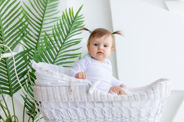Bebezinha linda sentada em um carrinho lindo com um macacão branco em casa