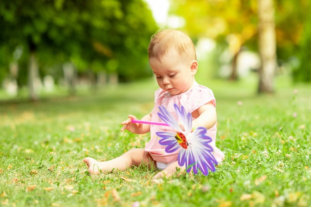 Bebezinho, 7 meses de idade, jogando em um gramado verde em uma roupa rosa, andando ao ar livre, desenvolvimento precoce de crianças até um ano