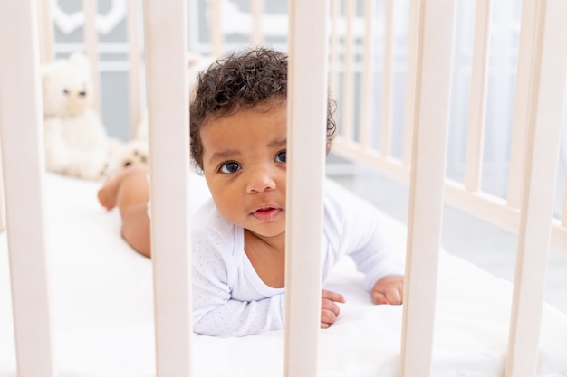 Bebezinho afro-americano fofo em uma cama branca para dormir parece de lado