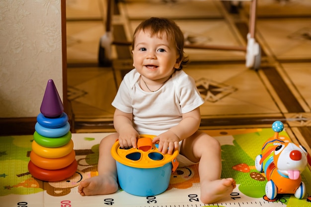 Bebezinho bonitinho brincando com brinquedos educativos coloridos no tapete de jogo no interior de casa