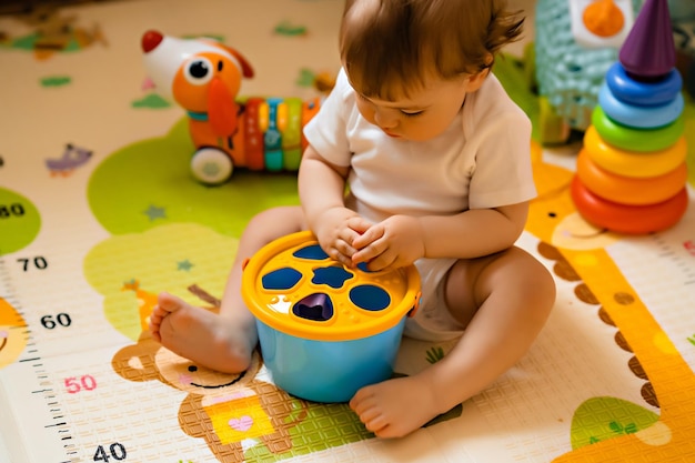 Bebezinho bonitinho brincando com brinquedos educativos coloridos no tapete de jogo no interior de casa