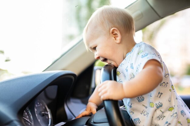 Bebezinho bonitinho dirigindo um carro grande, segurando o volante, sorrindo e olhando para a frente com interesse. Jogo e sonhos de infância. Copyspace