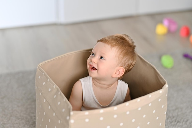 Bebezinho bonitinho sentado dentro de uma caixa com grandes caixas cheias de brinquedos no fundo, saindo do conceito