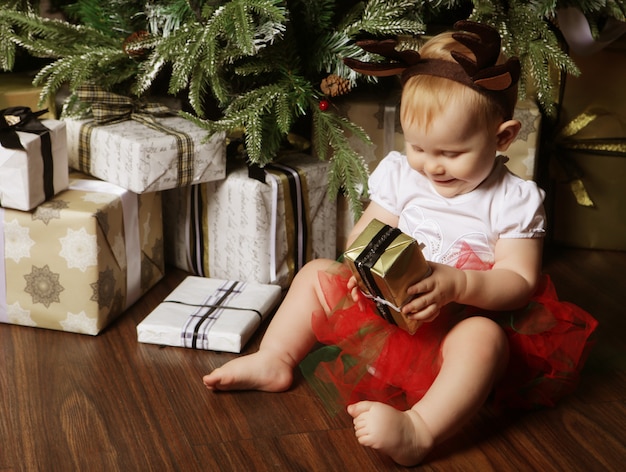 Bebezinho com a caixa de presente perto de decorar a árvore de natal