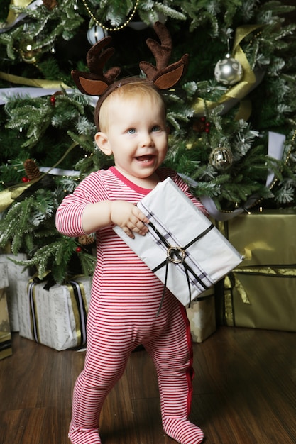 Bebezinho com a caixa de presente perto de decorar a árvore de natal