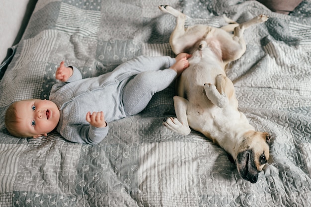 Bebezinho deitado com cachorro engraçado na cama.