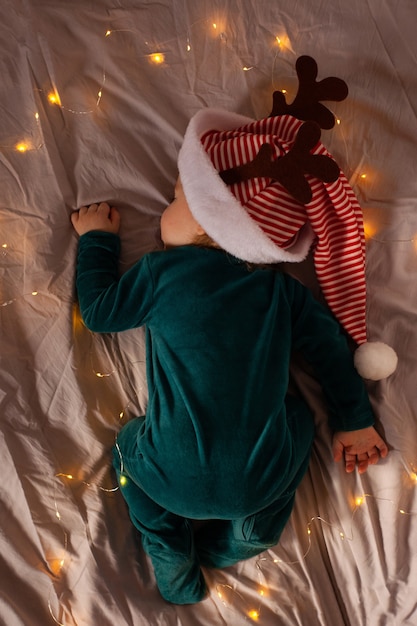 Bebezinho deitado na cama com uma fantasia de Natal e um chapéu com chifres de veado. Natal e ano novo.