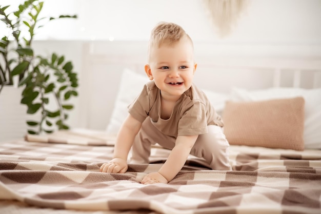 Bebezinho em roupas bege claro brincando em uma cama de luz em casa no quarto casa conforto felicidade da maternidade bebê em casa