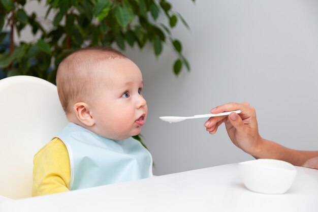 Bebezinho em roupas de cor, comer iogurte de colher, boca suja