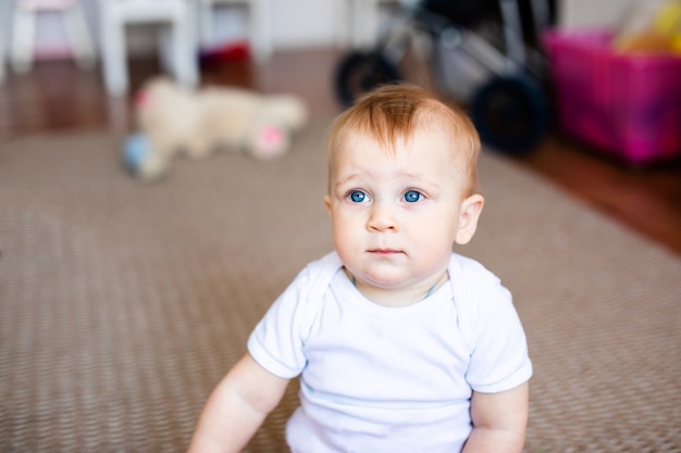 Bebezinho em t-shirt branca com um brinquedos no chão em casa