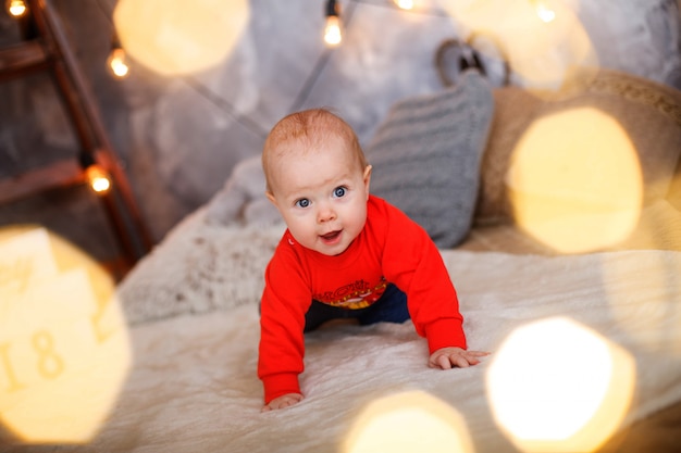 Bebezinho engraçado com um suéter vermelho. foto de bebê de ano novo. a criança aprende a engatinhar