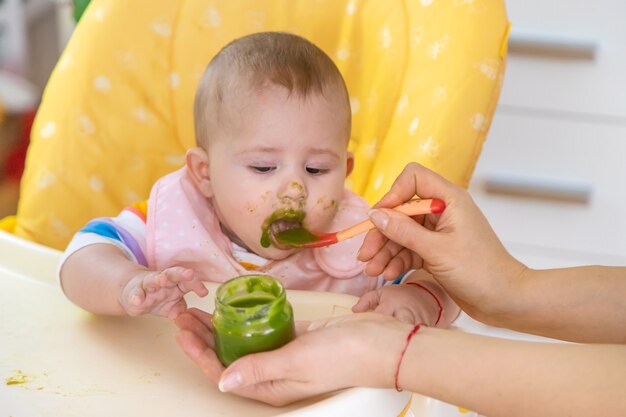 Bebezinho está comendo purê de vegetais de brócolis. Foco seletivo. Pessoas.