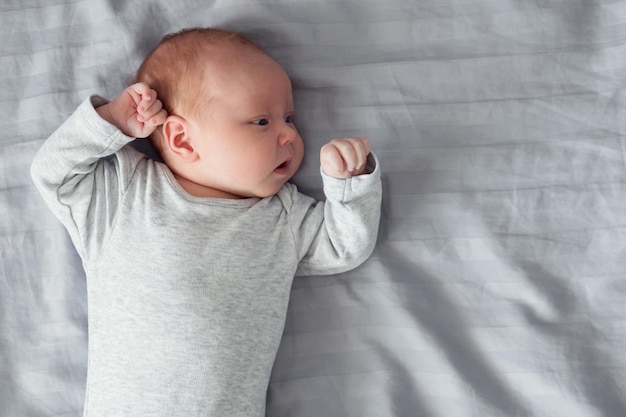 Bebezinho feminino em bodysuit cinza encontra-se na cama no quarto