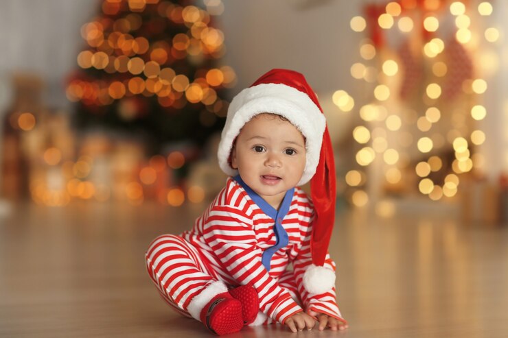 Foto bebezinho fofo com chapéu de papai noel no chão e luzes de natal borradas na superfície