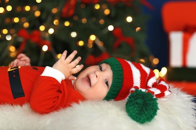 Bebezinho fofo fantasiado de Papai Noel deitado sobre um fundo desfocado de luzes de Natal