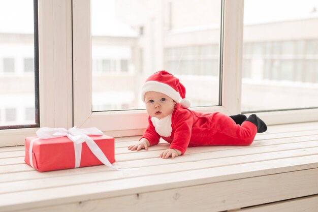 Bebezinho lindo celebra o Natal. Feriados de ano novo. Bebê com fantasia de Natal e chapéu de Papai Noel.