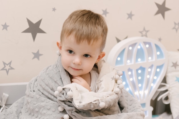 Bebezinho lindo sentado na sala de crianças em uma casa de cama de madeira com luzes noturnas em forma de um balão