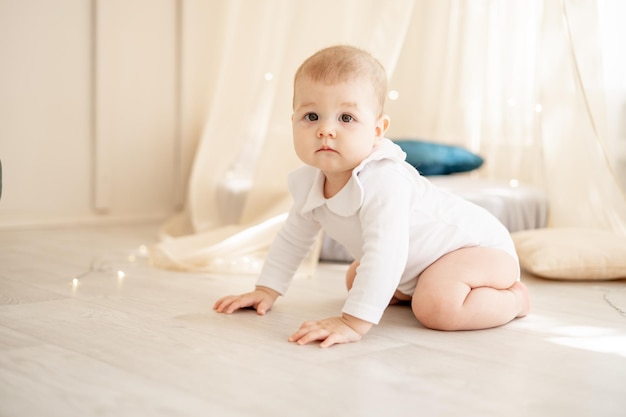 Bebezinho ou menina bonitinho em um quarto infantil brilhante com um wigwam em um macacão de algodão branco rastejando