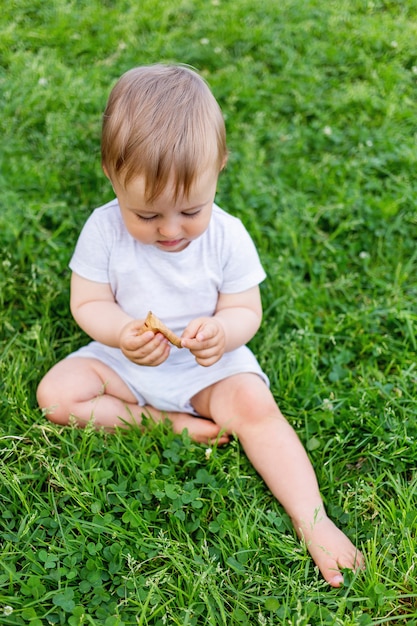 Bebezinho sentado na grama. Kid está olhando na folha caída. Atividade ao ar livre para o garoto.