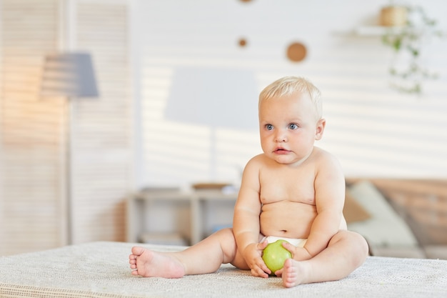 Bebezinho sentado na mesa da sala de estar segurando maçã verde fresca olhando para longe