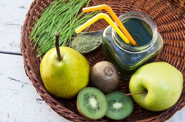 Foto bebida antioxidante da fruta verde fresca com brotos e pó do trigo na colher na placa de vime.