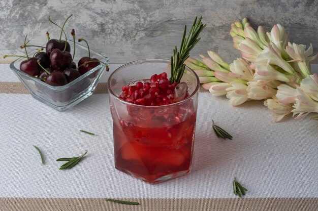 Bebida de arándanos con granada helada y una rama de romero acompañada de cerezas y flores