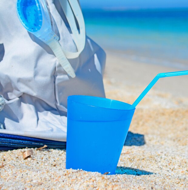 Bebida azul y bolsa de playa en una orilla blanca