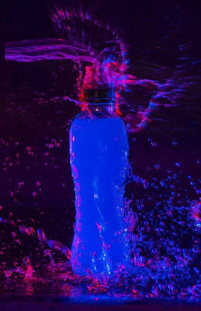 Foto bebida azul salpicando en botellas contra un fondo negro