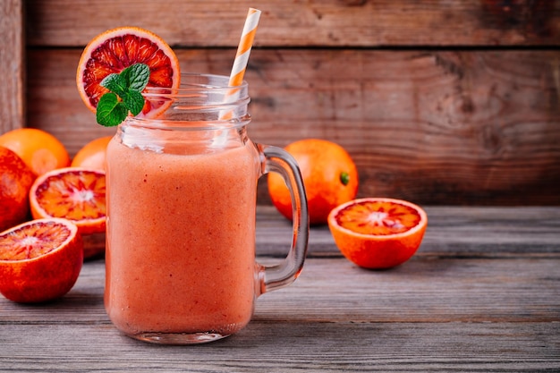 Bebida de batido fresco con naranjas de sangre de plátano y menta en un tarro de albañil sobre un fondo rústico de madera