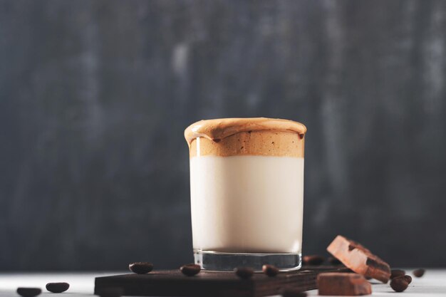 Bebida de café Dalgona batida en un vaso con leche, fondo oscuro.