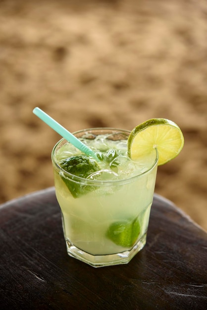 Bebida caipirinha brasileña en mesa de madera con fondo de playa de arena