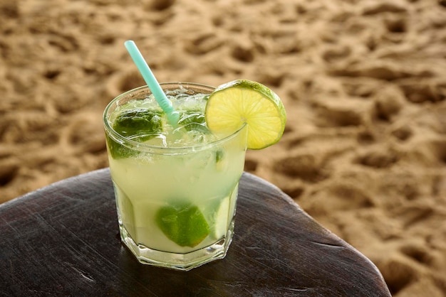 Bebida caipirinha brasileña en mesa de madera con fondo de playa de arena