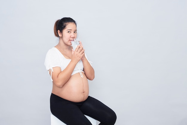 Bebida de calcio saludable. Mujer asiática joven embarazada sentada bebida de calcio saludable. Mujer asiática joven embarazada sentada sosteniendo un vaso de leche