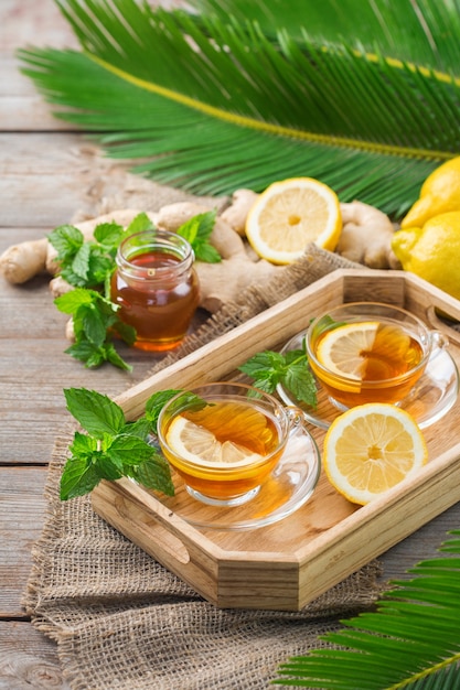 Bebida caliente en infusión de bebida en vaso para los días de otoño de invierno de gripe fría. Taza de té de jengibre con menta, limón y miel en una mesa de madera