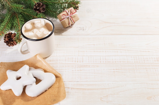 Bebida caliente de Navidad con malvaviscos en una taza de hierro y galletas de jengibre, sobre una mesa blanca. , vacaciones, copyspace.