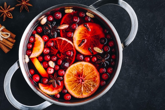 Bebida caliente de vino caliente con arándanos, naranjas, manzanas y especias sobre fondo de hormigón oscuro Vista superior espacio de copia