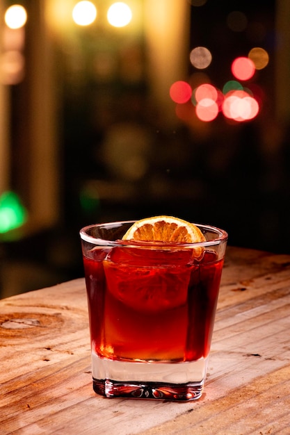 Bebida de campari negroni rojo con hielo líquido profesional sobre una mesa de madera rústica fondo de pub borroso