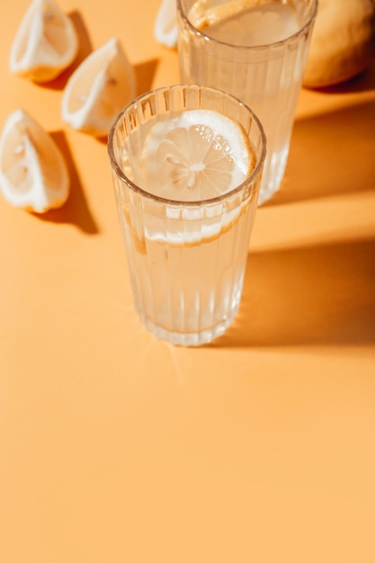 Foto bebida casera fermentada alcohólica o no alcohólica. limonada en vasos con rodaja de limón sobre fondo amarillo. sombra dura, tono beige.