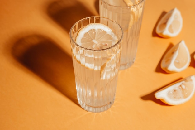 Bebida casera fermentada alcohólica o no alcohólica. Limonada en vasos con rodaja de limón sobre fondo amarillo. Sombra dura, tono beige