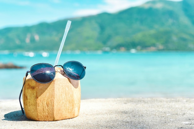 Bebida de coco con paja y gafas de sol en el fondo de la playa tropical