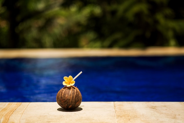 Bebida de coco tropical con flor amarilla, en el borde de la piscina