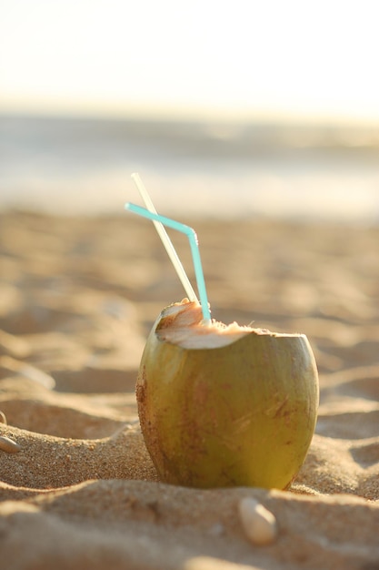 Bebida de coco verde con tubos de cóctel en la playa con fondo marino