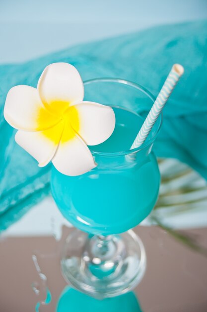 Bebida de cóctel tropical exótico Curacao azul en un vaso con flor de frangipani Plumeria.