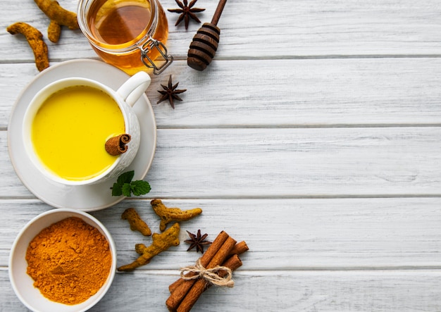 Bebida com leite de açafrão amarelo. Leite dourado com canela, açafrão, gengibre e mel sobre fundo branco de madeira.