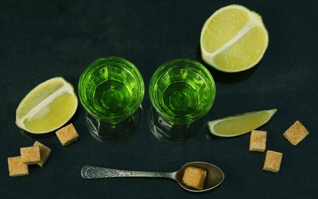 bebida de absinto verde no fundo preto com açúcar e limão